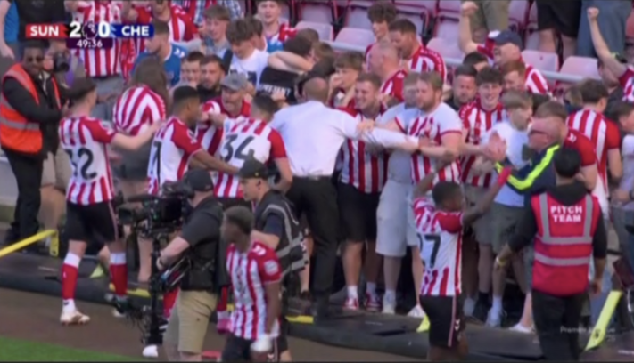 Sunderland fans celebrating on the field, wearing red and white striped jerseys, surrounded by security.