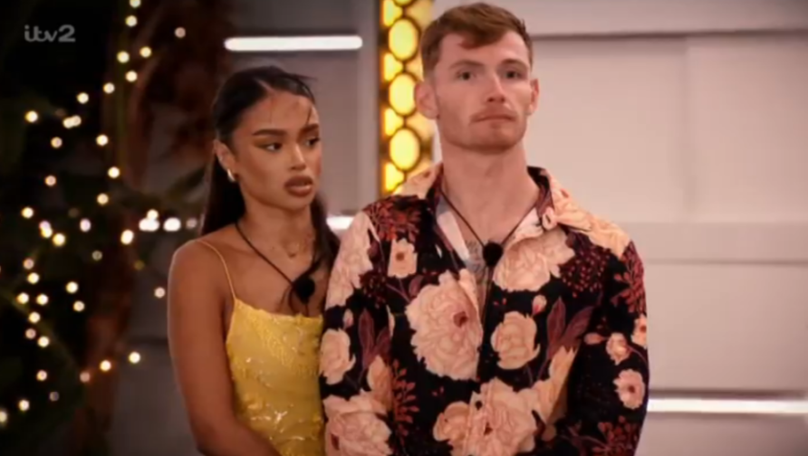 A man in a floral shirt and a woman in a yellow dress looking concerned.