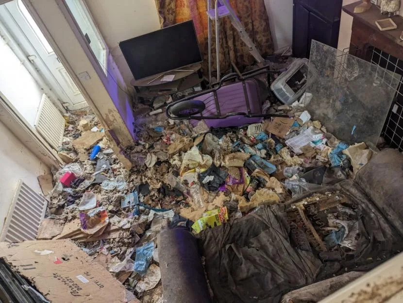 A cluttered room filled with rubbish, debris, and overturned furniture, covered in animal faeces and waste.