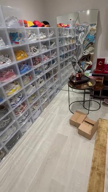 A large room with clear shoe boxes displaying numerous sneakers, a distorted mirror, and two small tables with items, including open cardboard boxes on the floor.
