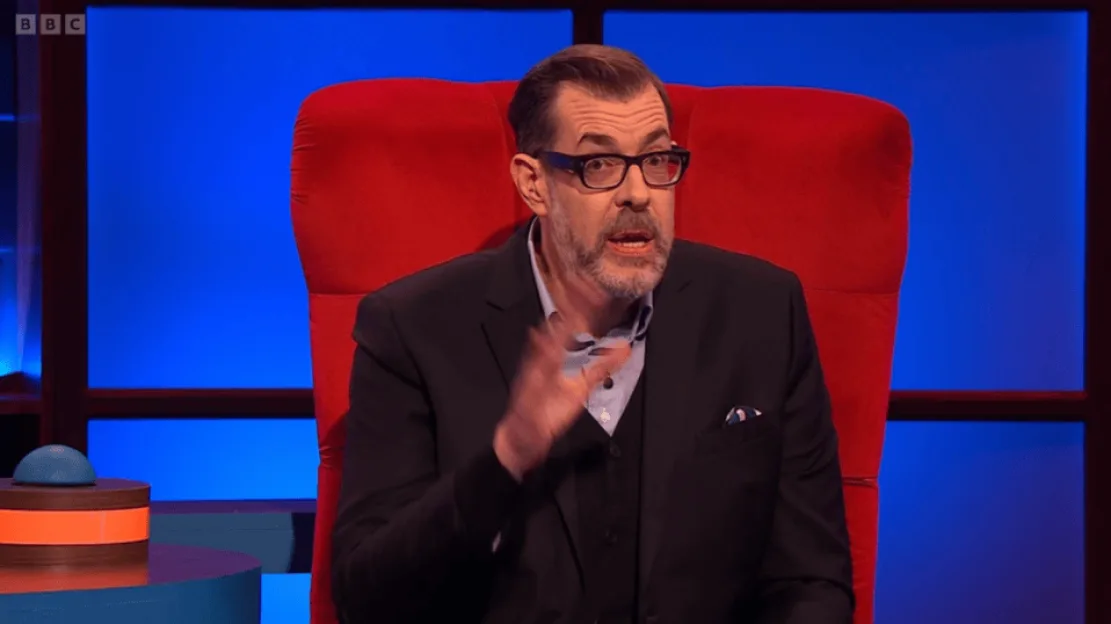 Richard Osman sitting in a red chair and talking.