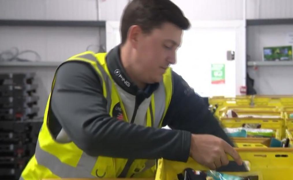 A man in a high-visibility vest sorting items into yellow bins.