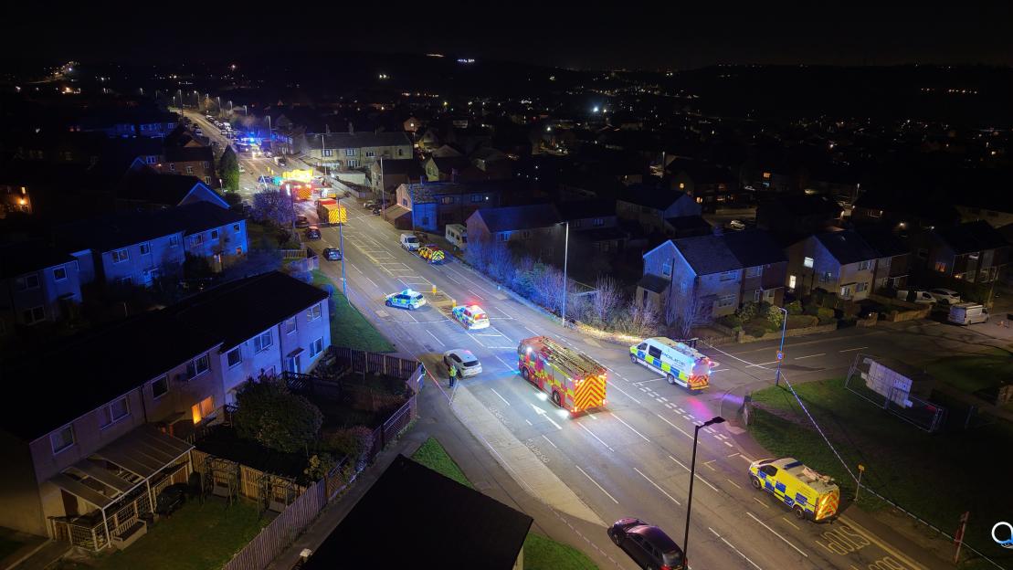 Aerial night shot of multiple emergency vehicles at a crash site on a street lined with houses.