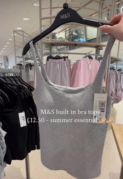 A hand holding a gray M&S built-in bra top on a hanger in a store, with the text "M&S built in bra tops £12.50 - summer essential" overlaid.