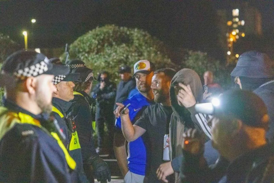 A protestor pours a vodka drink in front of police officers during an anti-migrant protest in Gosport, England.