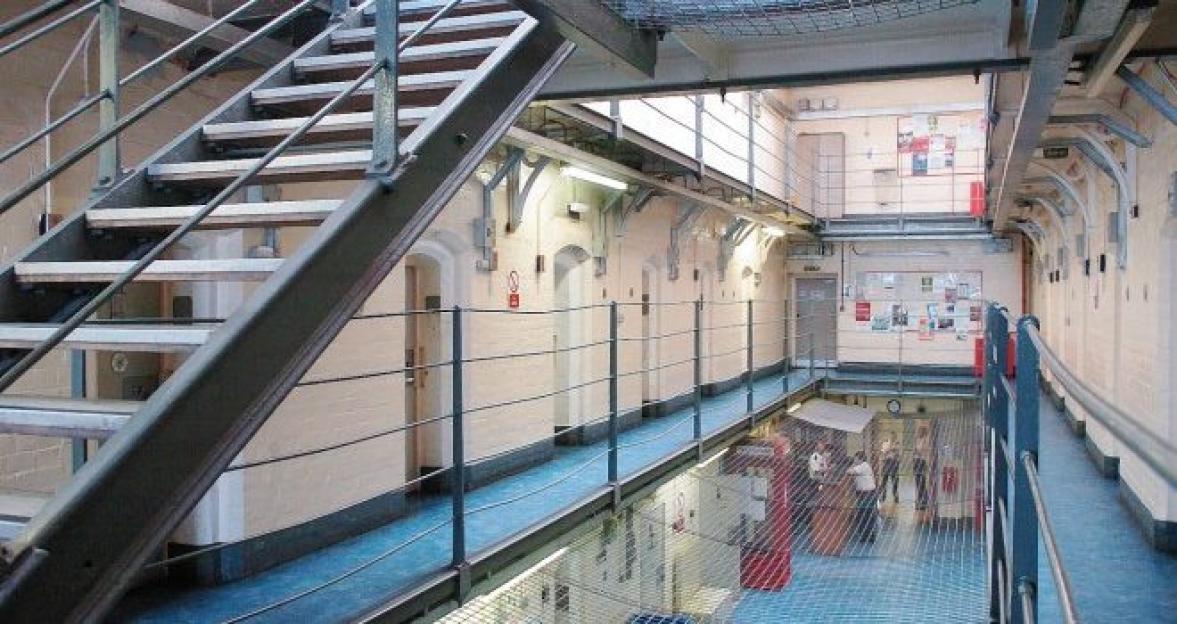 Interior of a multi-story prison with rows of cell doors, metal staircases, and a wire mesh covering the ground floor.