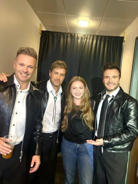 Emily Webber posing with three members of Westlife, who are all wearing black leather jackets.