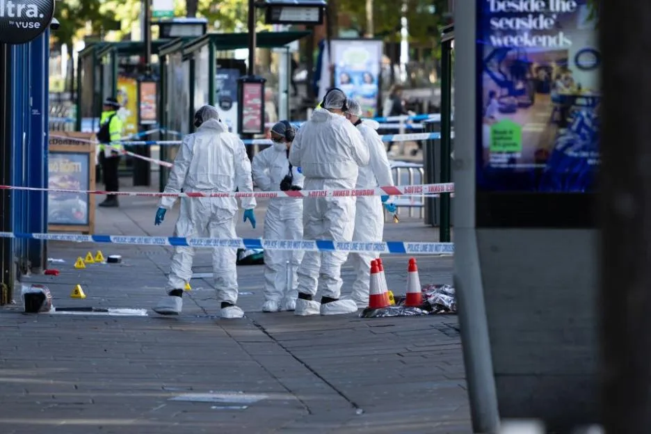 Forensics team investigating a weapon at a crime scene behind police tape in Nottingham City Centre.