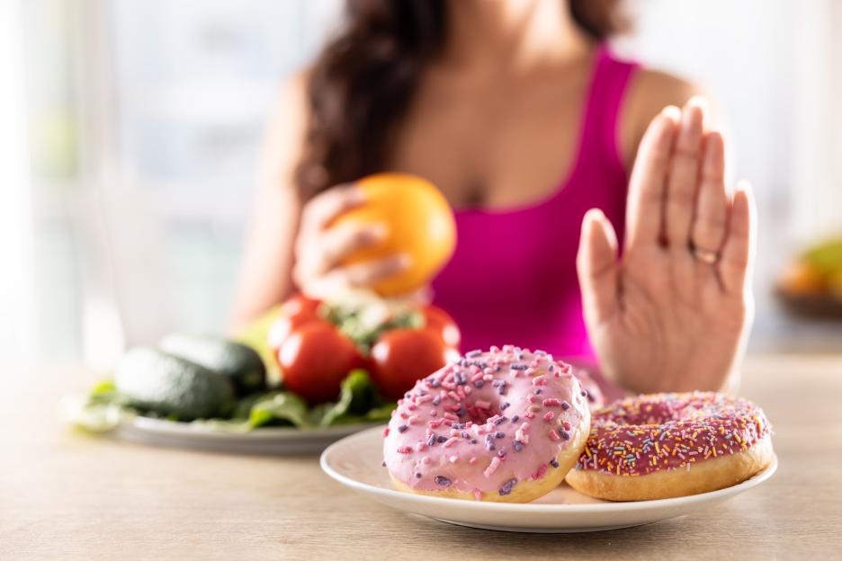 Woman in pink top refusing donuts and choosing healthy vegetables.