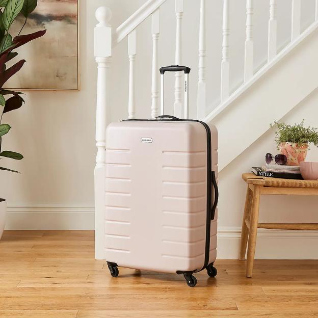 A pink Constellation Skyline hard shell suitcase on a wooden floor next to a white staircase.