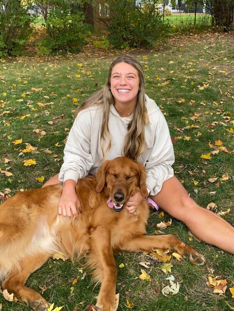 Lex Banach smiling and petting her golden retriever outside.