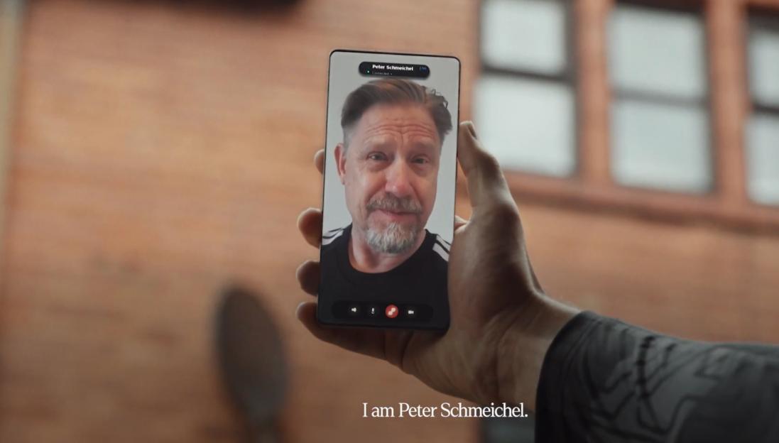 A video call with Peter Schmeichel on a smartphone held by a person with a tattoo on their arm.