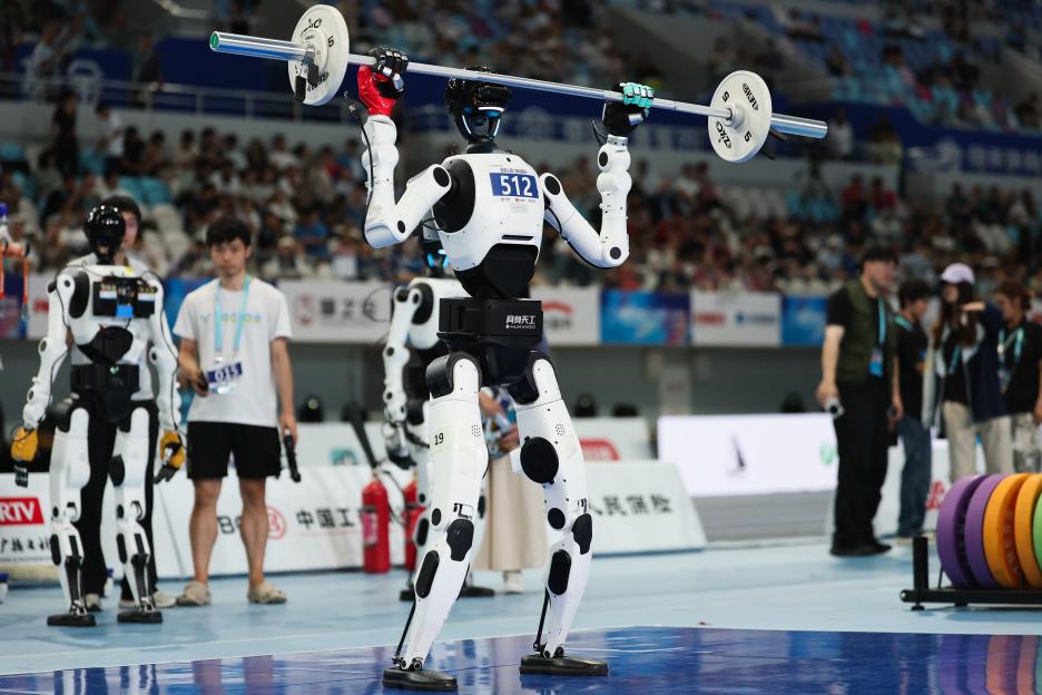 A humanoid robot wearing number 512, with a white body and black joints, performs a weightlifting overhead press at the 2nd World Humanoid Robot Games.