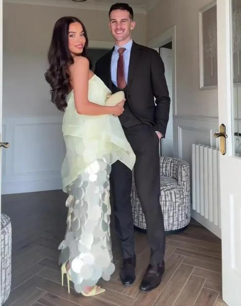 A smiling woman in a light green, sequined dress and a man in a suit standing in a hallway.