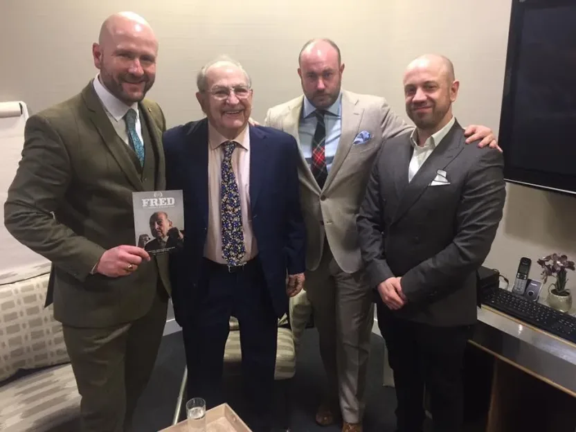 Four men standing together, with the man on the far left holding a magazine titled "FRED".