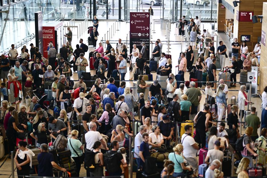 Passengers queue at a check-in counter in Terminal 1 of Berlin Brandenburg BER Airport due to cyber-related disruption.