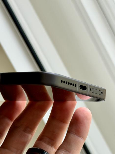 Close-up of a hand holding a black Xiaomi phone, showing the speaker grills and SIM card slot on the side.