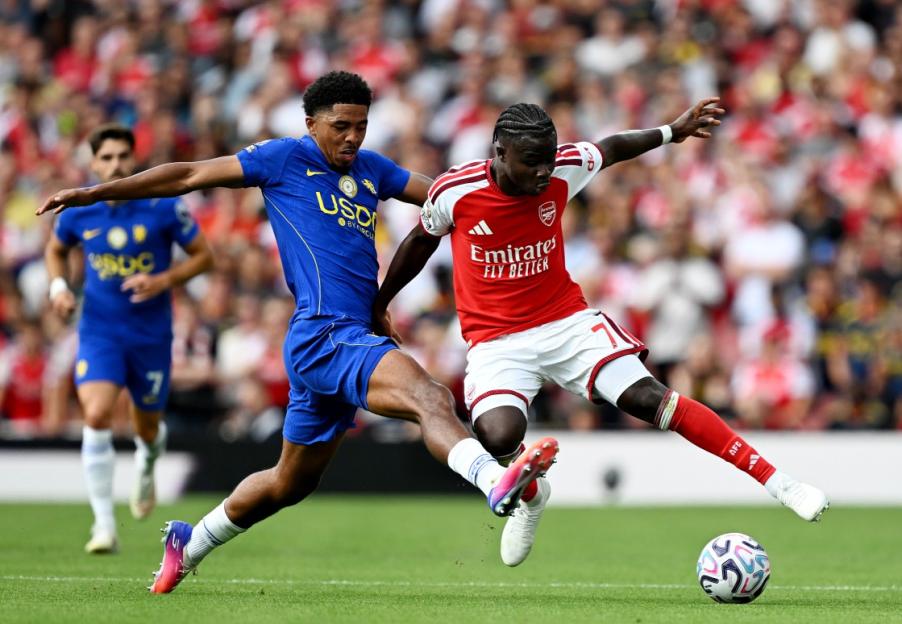 Two soccer players, one in red and one in blue, battle for the ball during a Premier League match.