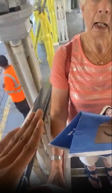 An elderly woman is blocked from climbing stairs at a train station.