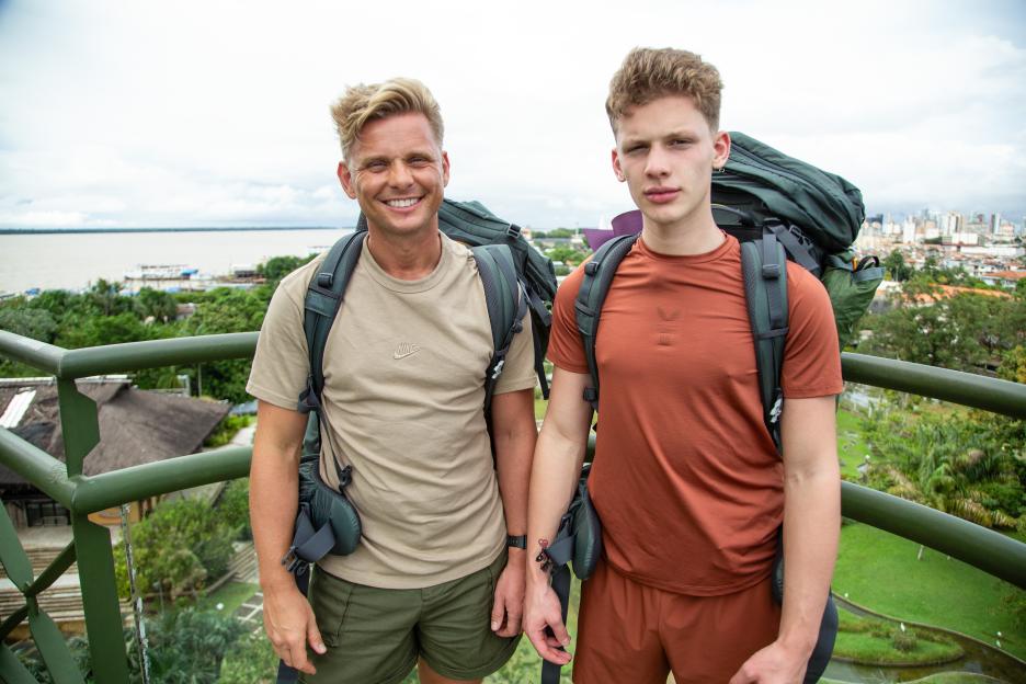 Jeff and Freddy Brazier posing in hiking gear with a cityscape and river in the background.