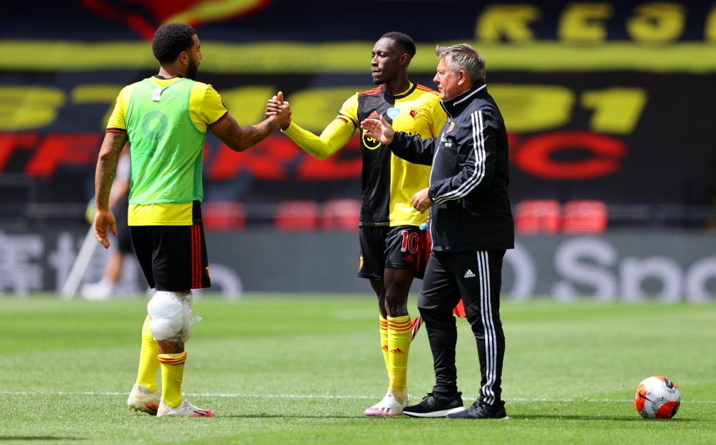 Two soccer players and a coach on a field at Vicarage Road during a match between Watford FC and Newcastle United.