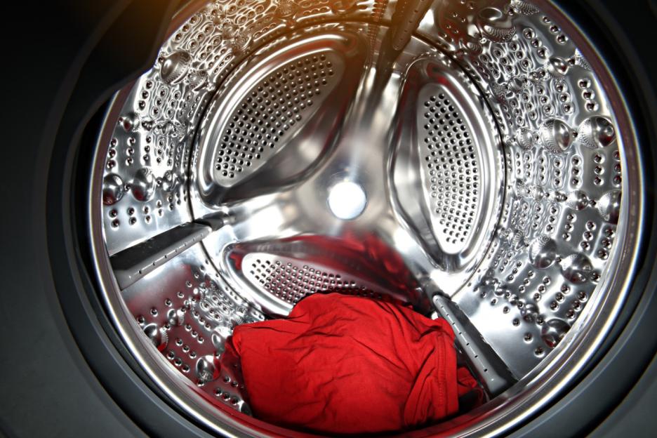 View inside a tumble dryer or washing machine drum with red clothes inside.