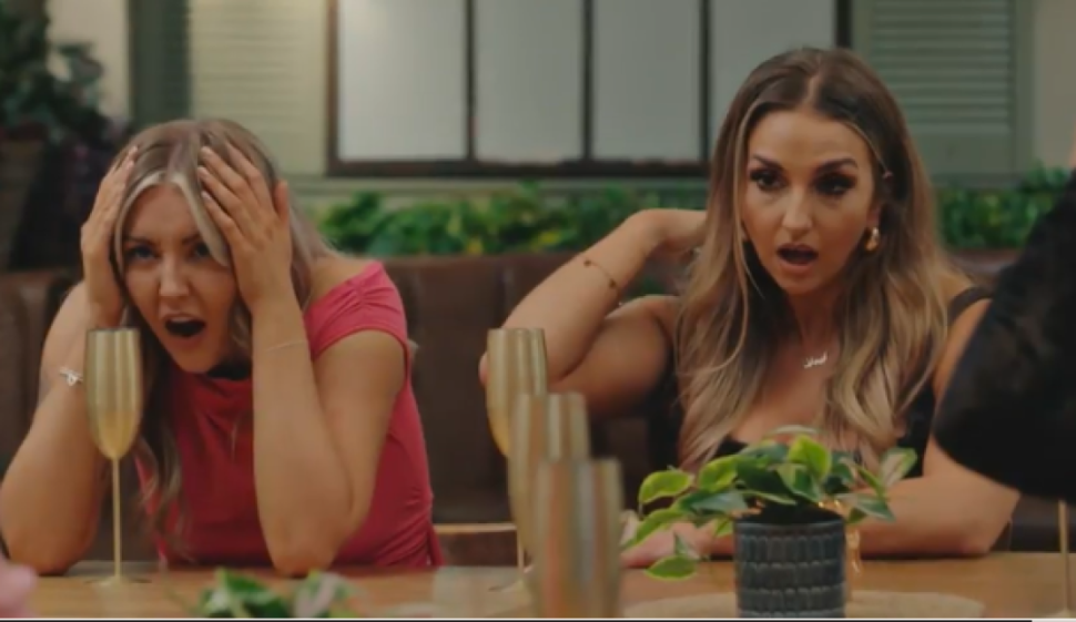 Two women, one in pink and one in black, reacting with shock and hands to their heads.