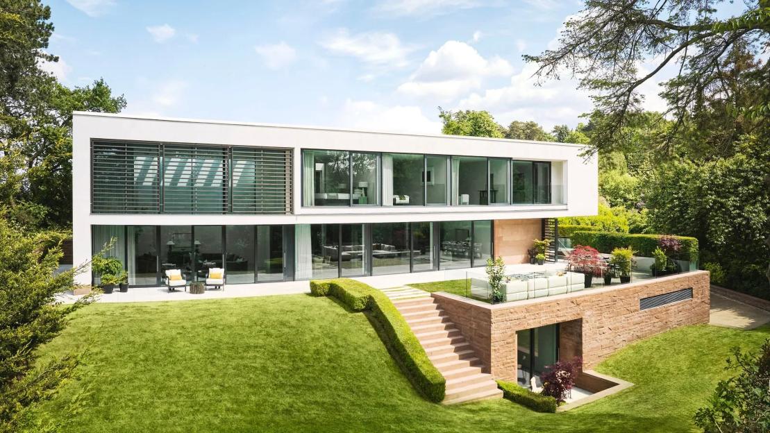 Exterior of the luxury Omaze Prize house in Cheshire, with large windows, green lawns, and a terraced patio area.