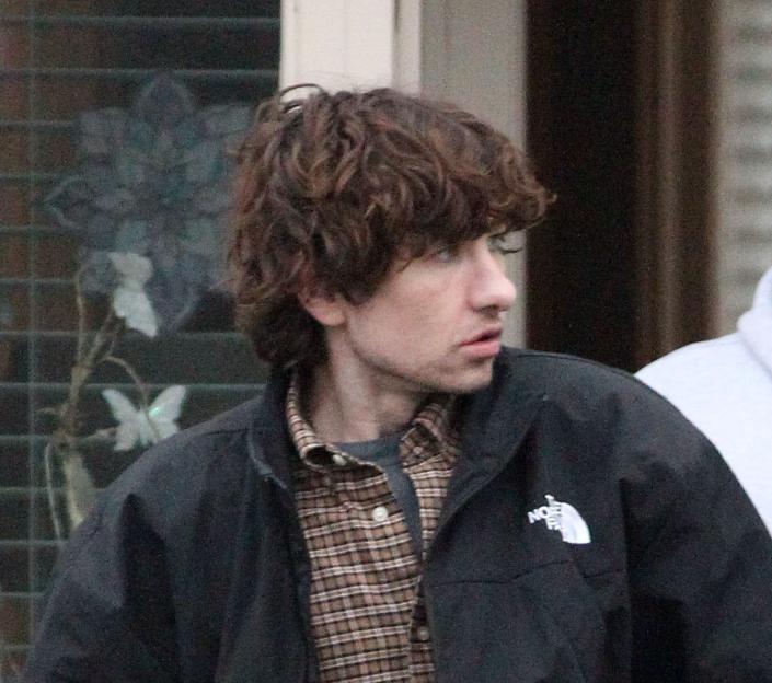 Actor Barry Keoghan (left) in character as Josh wearing a black jacket, plaid shirt, jeans, and brown boots, walks away from a doorway followed by another man.
