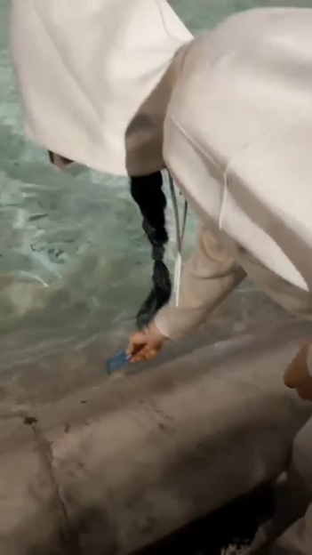 A person in a white hoodie dips a credit card into the Trevi Fountain.