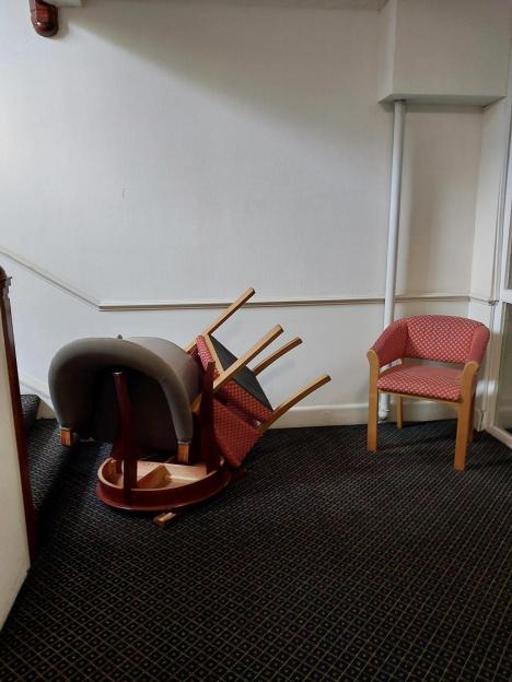 Damaged hotel furniture including an overturned table, a chair lying on its side, and another chair upright.