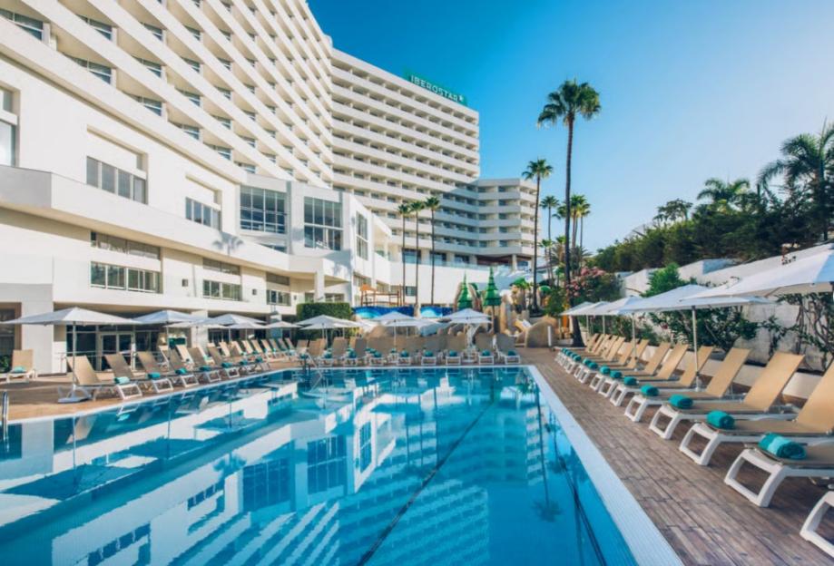 The Iberostar Bouganville Playa hotel in Costa Adeje, Tenerife, with its outdoor pool, lounge chairs, and palm trees.