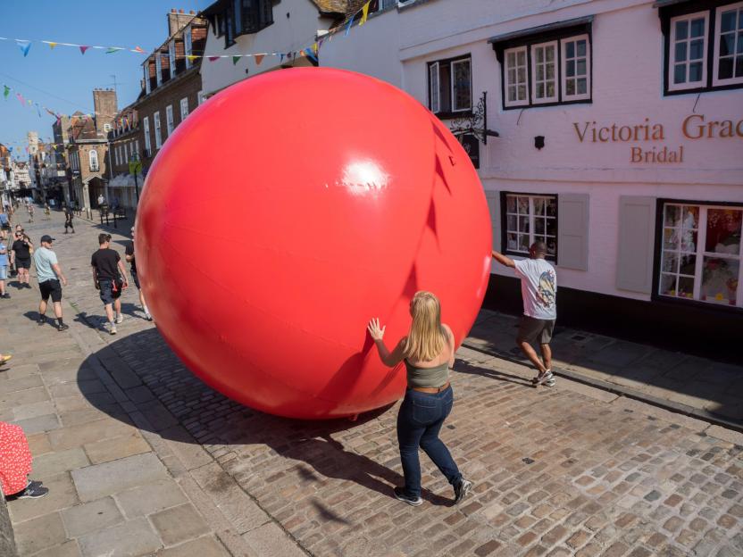 People pushing a giant red ball down a cobbled street in Canterbury.