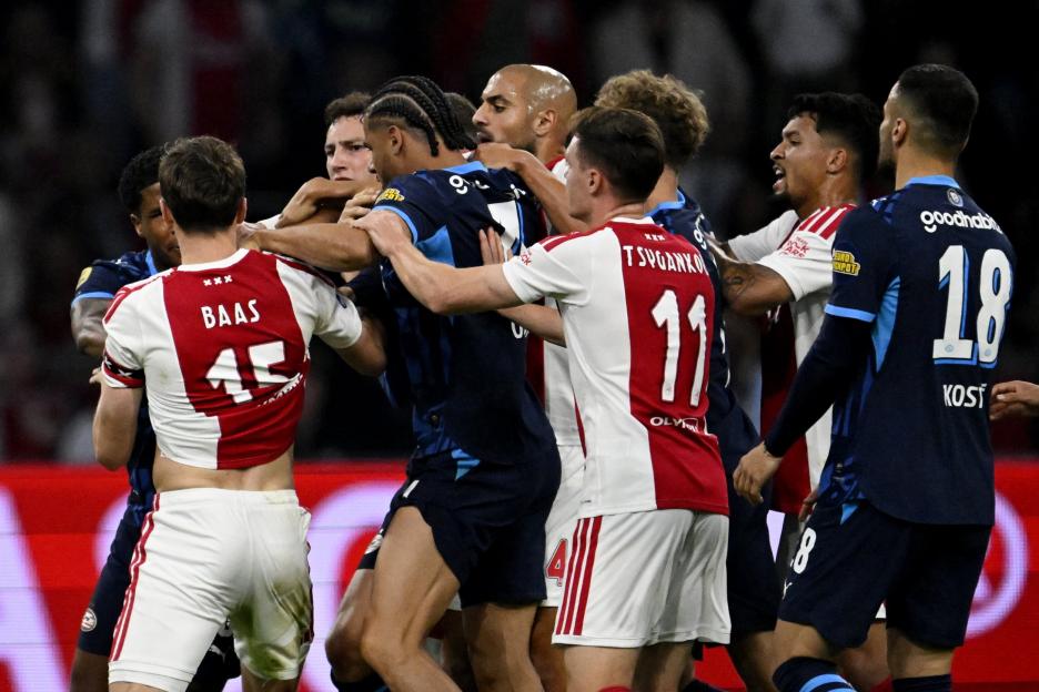 Football players from AFC Ajax and PSV pushing and grabbing each other during a confrontation on the field.