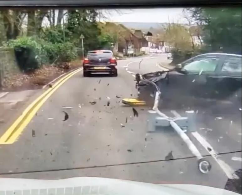 A black car on the road with debris from a collision, while another black car drives away in the distance.