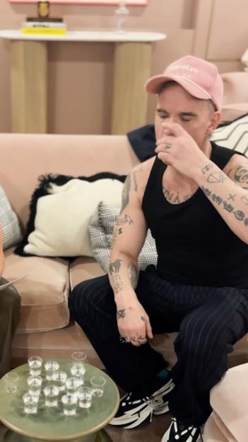 Robbie Williams playing a Truth or Dare drinking game with shots on a coffee table.