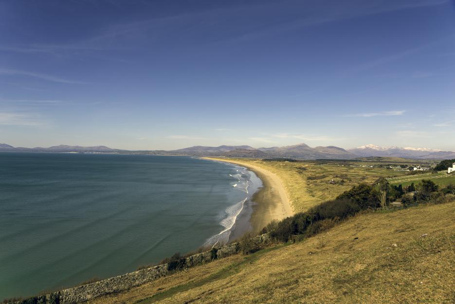 Harlech Beach and Cardigan Bay with mountains in the background under a blue sky.