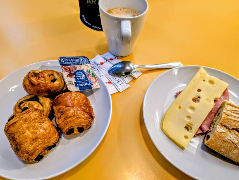 Breakfast with pastries, cheese, ham, bread, and coffee on a yellow table.