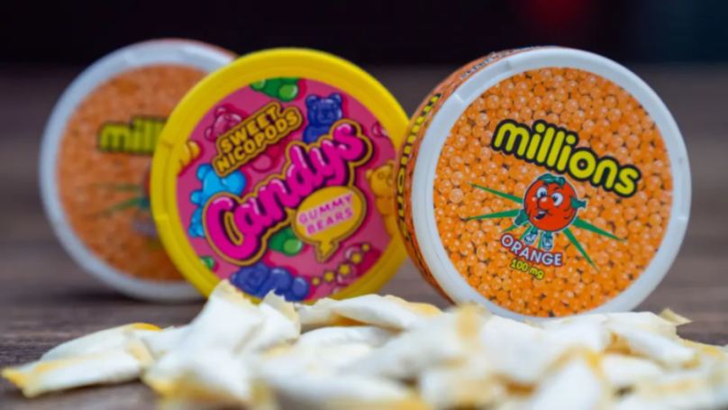 Nicotine patches packaged like "Millions" sweets, with orange "Orange 100 mg" and pink "Candys Gummy Bears" flavors shown, and a pile of discarded patches in the foreground.