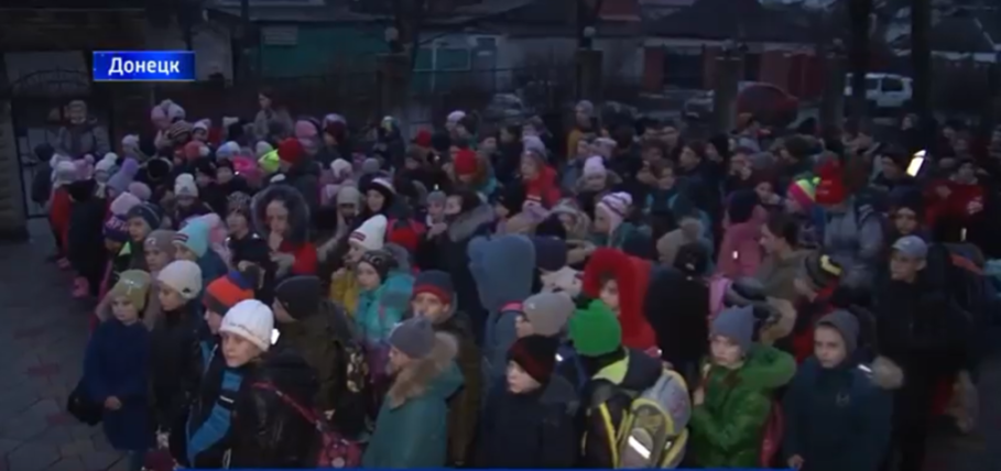 A large group of children and some adults, many bundled in winter clothing, standing outdoors in Donetsk.