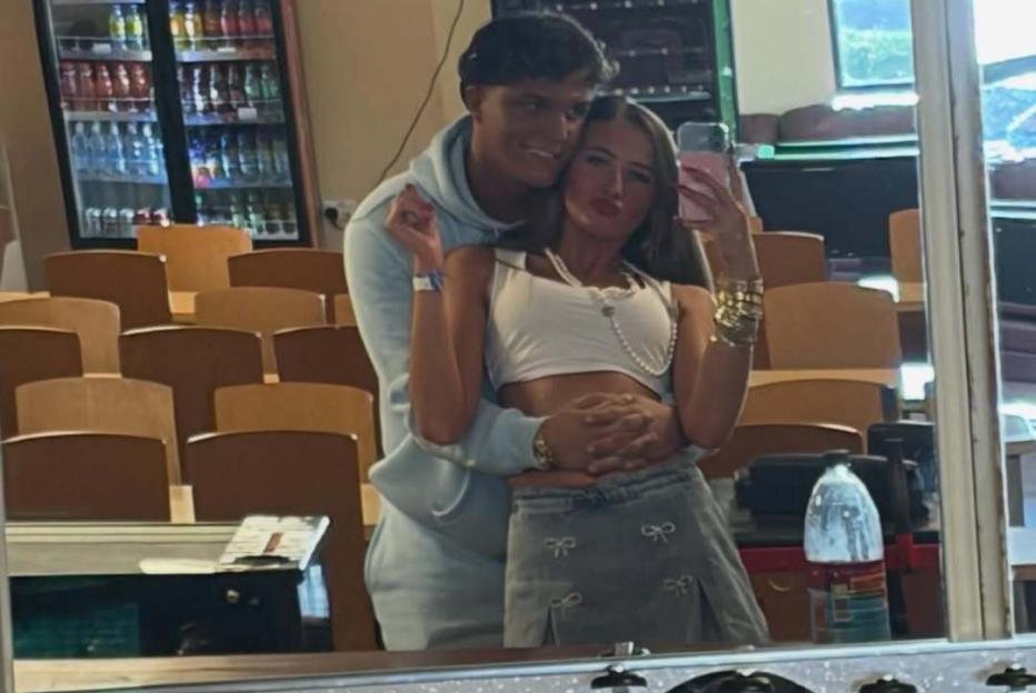 A couple poses in a mirror selfie, the man hugging the woman from behind.