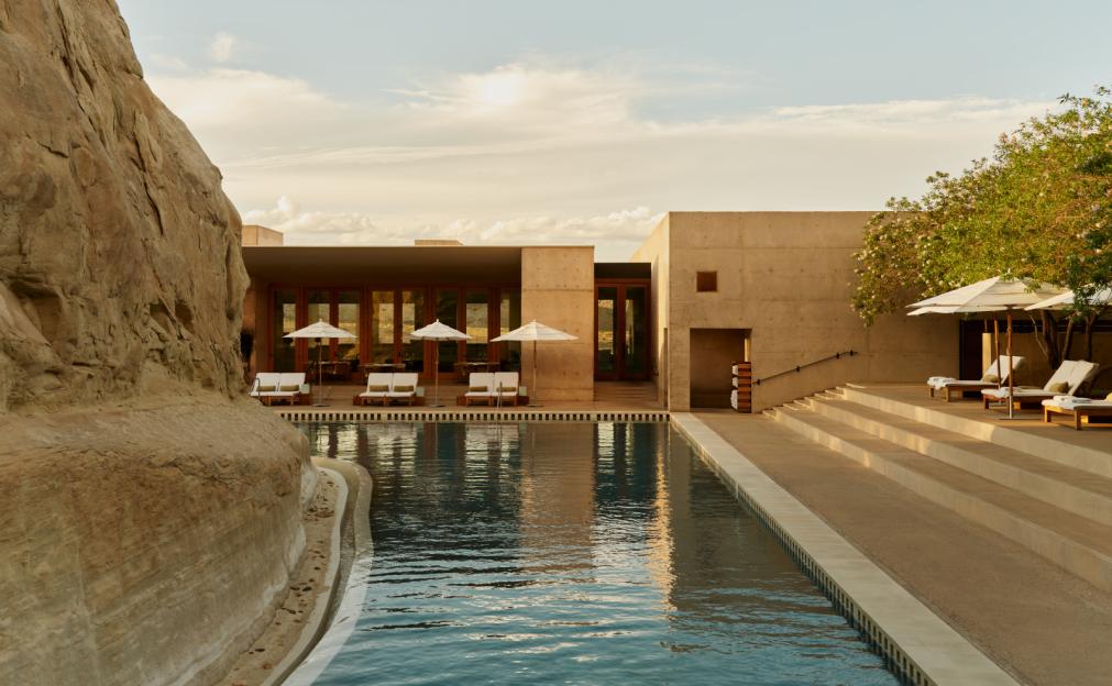 The pool area at Amangiri Hotel in Utah, featuring a rock formation on the left, a large swimming pool, and concrete buildings with lounge chairs and umbrellas.