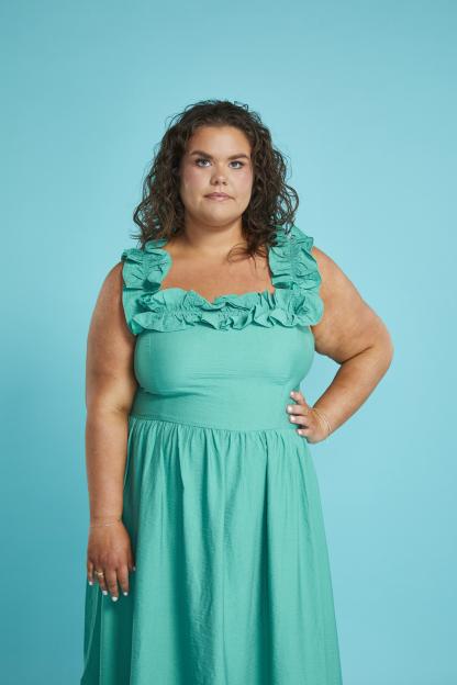 Woman in teal dress against teal background.