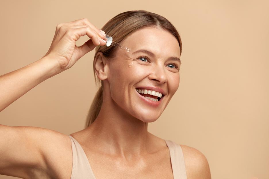 Woman dropping serum on her face for hydrated, glowing, and healthy skin.
