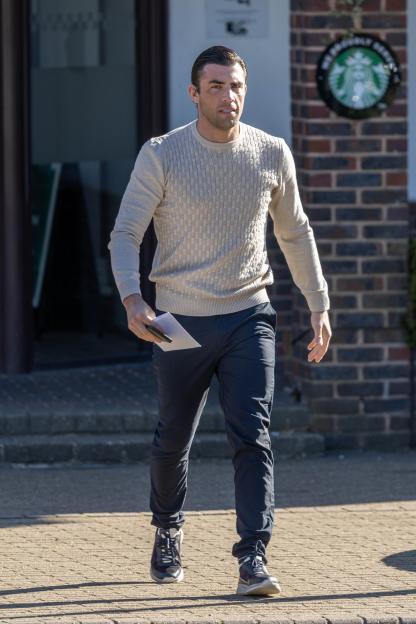 Jack Fincham walking on a paved surface, looking towards the right, with a Starbucks logo visible in the background.