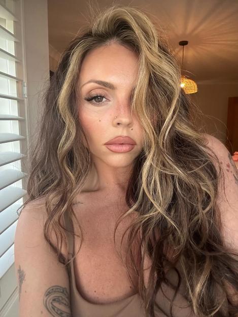 Jesy Nelson with long wavy brown and blonde hair, wearing a tan top.