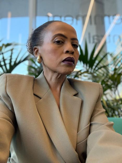 Charmaine Masoeu looking directly at the camera, wearing a light brown blazer and dark lipstick.