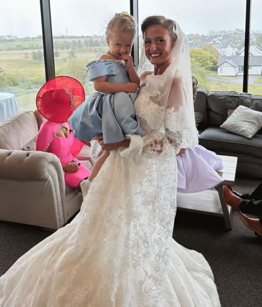 Molly-Mae's daughter Bambi Fury as a bridesmaid, held by a woman in a wedding dress.
