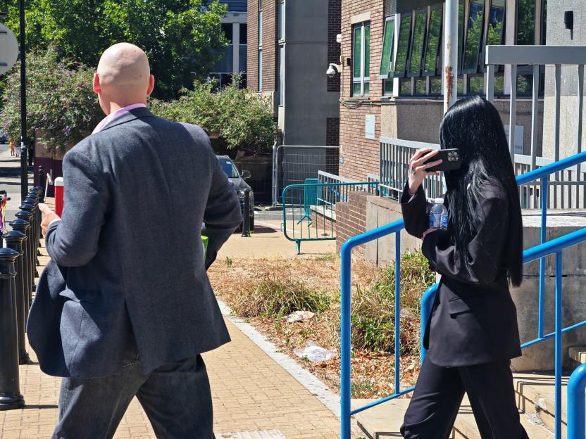 A man with a bald head and a woman with long black hair filming him with a phone.