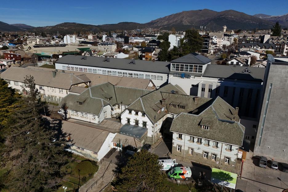 Aerial view of a hospital complex and surrounding town with mountains in the background.